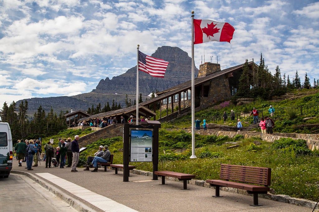 Visitors gather along the walkways outside the Logan Pass Visitor Center beneath American and Canadian flags in Glacier National Park.