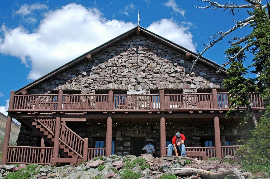 Hikers rest in front of the stone facade and wooden balcony of Granite Park Chalet in Glacier National Park.